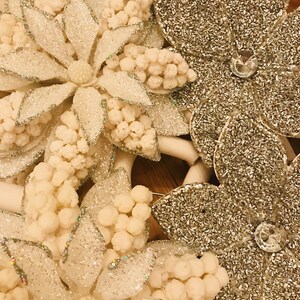 May include: A close-up of a white and silver glittery Christmas wreath with white flowers and silver glitter accents.