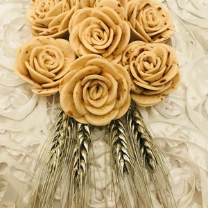 May include: A bouquet of beige fabric roses with silver wheat stalks. The roses are made from fabric and are arranged in a circular shape. The wheat stalks are arranged around the roses.