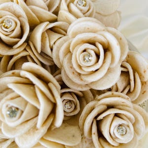 Può includere: Un bouquet di rose bianche di tortilla con strass al centro di ogni fiore.