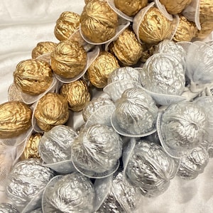 May include: A decorative cluster of whole walnuts individually encased in white mesh netting. The walnuts are painted in metallic gold and silver finishes, arranged in a dense, overlapping formation that highlights the textured shells.