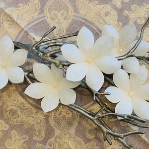 May include: A set of five white paper flowers with a pearl centre, arranged on a silver branch. The flowers are delicate and have a slightly textured surface.