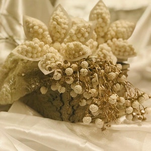 May include: A white decorative box with a white floral arrangement and white and gold accents. The box is sitting on a white satin fabric.