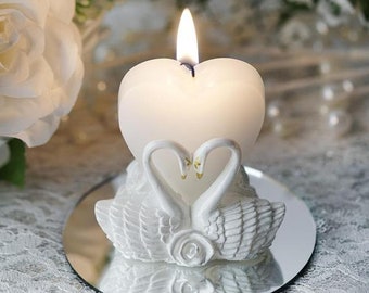 May include: White heart-shaped candle with a pair of white swans on a mirrored base. The candle is lit and the swans are facing each other.