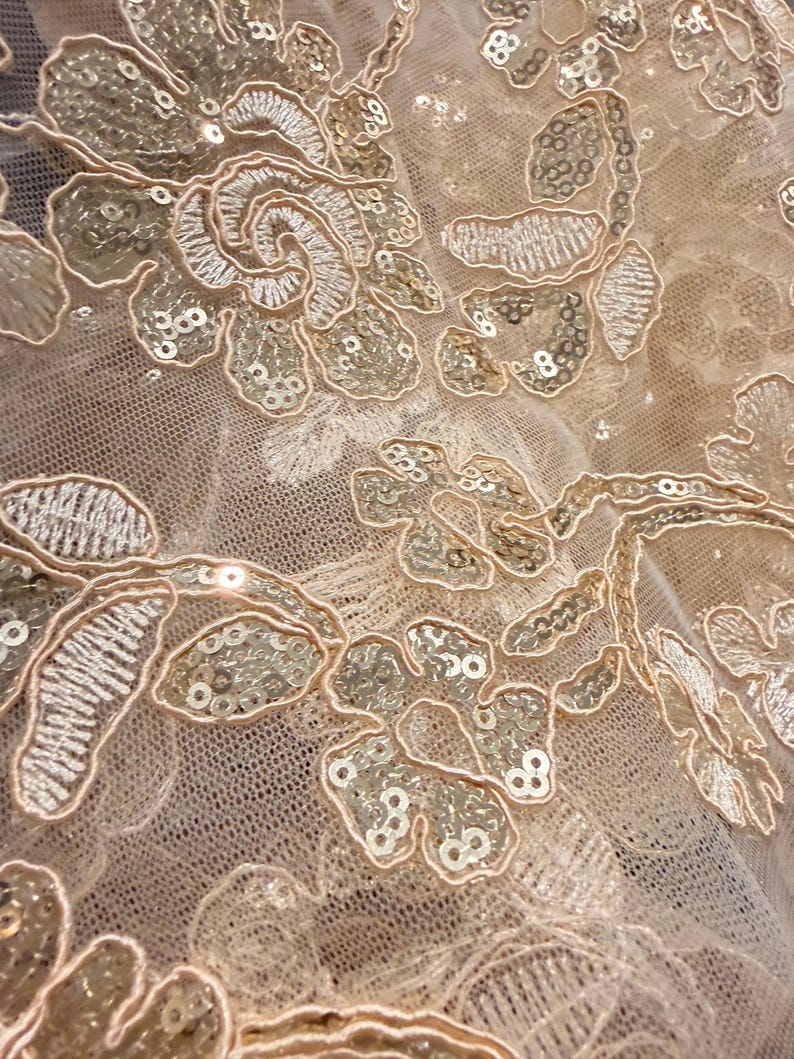 May include: A sheer beige mesh fabric featuring intricate floral embroidery in a matching thread color. The design is embellished with small, reflective sequins that follow the contours of the flower petals and leaves, creating a textured surface.