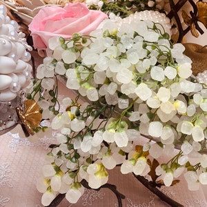May include: A decorative wedding centrepiece featuring a cluster of white sugar crystals on a branch with a pink rose and white pearl accents.