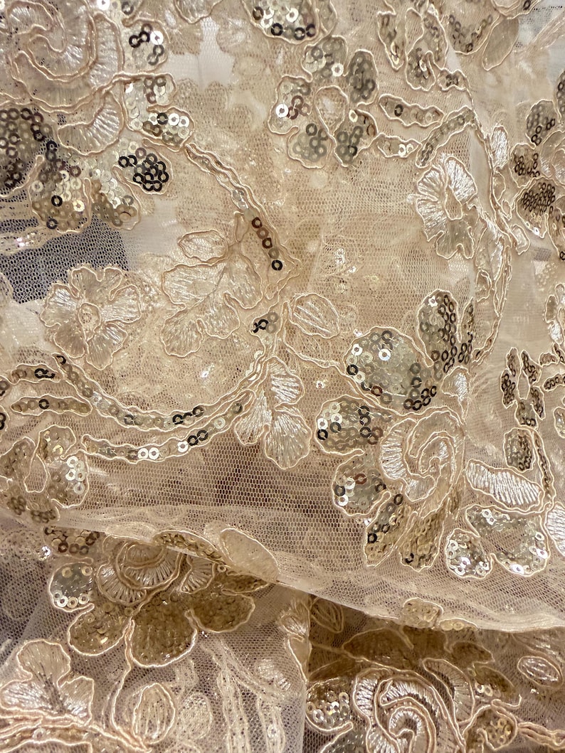 May include: A sheer champagne-colored mesh fabric featuring intricate floral embroidery with matching thread and scattered metallic sequins. The delicate netting base is adorned with repeating botanical patterns that create a textured surface.