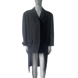 Può includere: Un blazer nero con schiena lunga e spaccata. Il blazer ha tre bottoni, due tasche anteriori e revers a lancia. Le maniche sono risvoltate. Il blazer è esposto su un manichino.