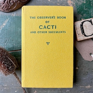 May include: A yellow hardcover book titled The Observer's Book of Cacti and Other Succulents with dark green text printed on the front cover. The book has a textured surface and a small triangular logo centered below the title text.