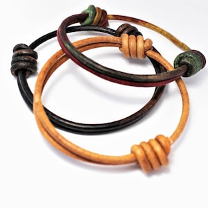 May include: Three leather bracelets with knotted ends. The bracelets are in shades of brown, black, and green.