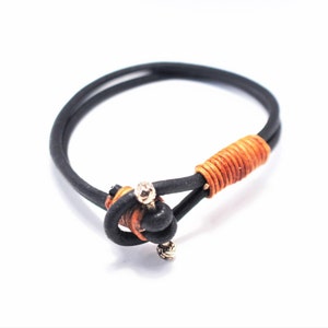 May include: A black leather bracelet with a brown leather wrap and a gold metal accent.