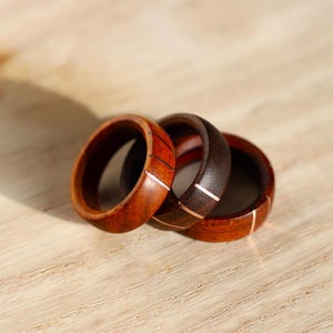 May include: Three wooden rings with copper inlay. The rings are stacked on top of each other. The rings are made of dark wood and light wood.