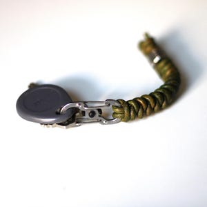 Puede incluir: Un llavero de cuero trenzado verde con un mosquetón plateado y un llavero gris.