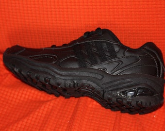 May include: Black athletic shoe with a chunky sole and a textured tread. The shoe has a leather upper with three stripes on the side. The shoe is set against an orange background.