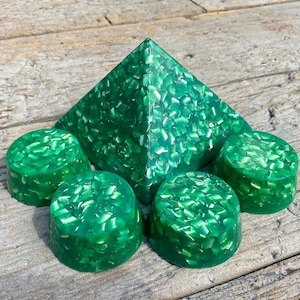 Puede incluir: Un conjunto de cinco formas de pirámide y redondas de resina verde con un acabado brillante y brillante. La pirámide es más grande que las cuatro formas redondas.
