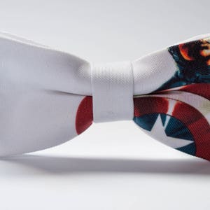 Puede incluir: Pajarita blanca con una imagen impresa del escudo y la cara del Capitán América.