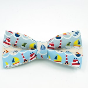 May include: A blue bow tie with a white background and a pattern of sailboats, lighthouses, and the text "at the sea".