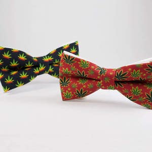 Puede incluir: Dos pajaritas con un patrón de hojas. Una pajarita es negra con hojas verdes y amarillas. La otra pajarita es roja con hojas verdes y amarillas.