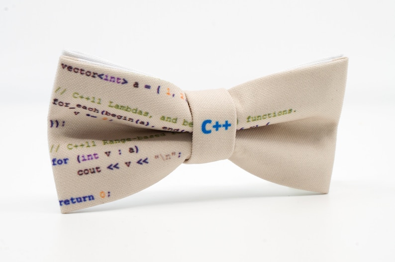 K&ouml;nnte beinhalten: Ein beiger Fliege mit wei&szlig;em Rand und einem C++-Logo in Blau. Die Fliege ist mit C++-Code bedruckt.