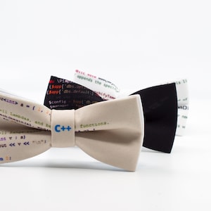 Könnte beinhalten: Drei Fliegen mit einem Coding-Thema. Die Fliegen sind beige, schwarz und weiß mit Code bedruckt. Die beige Fliege hat den Text "C++" aufgedruckt.