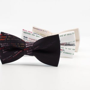 Può includere: Tre papillon con sfondo nero, bianco e crema. Ogni papillon presenta un codice diverso stampato sul tessuto. I frammenti di codice includono testo come "Node crunchif", "Sconfined.comsconfi" e "end of this ti".