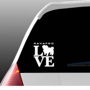 May include: White vinyl car decal featuring the word "HAVAPOO" above the word "LOVE" with a silhouette of a Havanese dog replacing the "O". The decal is displayed on a car window.