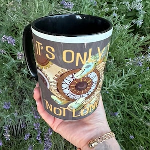May include: Black coffee mug with a white rim and a graphic of gears and an eye with the text "It's only you not long" printed on it.