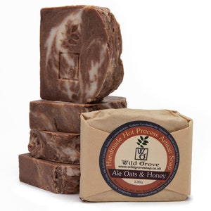 May include: Four bars of brown and white marbled soap stacked on top of each other. The top bar has a brown stamp with the words "Wild Grove" and "Ale Oats & Honey". The soap is wrapped in brown paper with the words "Handmade Hot Process Artisan Soap" printed on it.