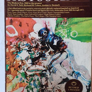 May include: A hardcover book titled The Sports Encyclopedia: PRO FOOTBALL, The Modern Era, 1960 to the present by David S. Neft, Richard M. Cohen, and Jordan A. Deutsch. The cover features a colorful, abstract watercolor illustration of football players.