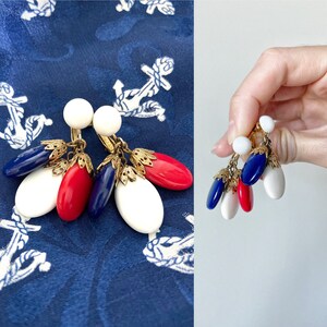 May include: A pair of clip-on earrings with red, white, and blue teardrop-shaped beads. The earrings are made of gold-toned metal and have a dangling design.
