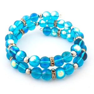 May include: A spiral wrap bracelet featuring iridescent blue glass beads. The bracelet has two strands of beads, separated by silver-colored spacers and embellished with rhinestone-studded bands. The beads have a translucent quality, reflecting light.
