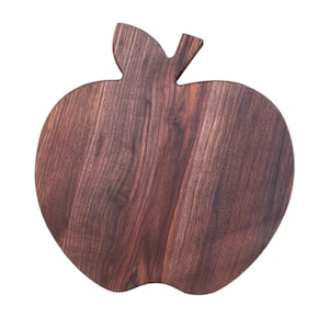 May include: A wooden apple-shaped cutting board with a leaf and stem detail. The board is made of dark brown wood with visible grain patterns. The design is a decorative and functional kitchen item.