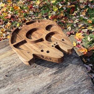 May include: A wooden serving tray shaped like the Millennium Falcon from Star Wars. The tray has multiple compartments and is engraved with the initials "N.C.W."
