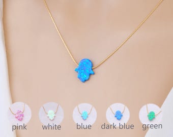 Peut inclure: Un collier en chaîne dorée avec un pendentif en forme de main de Hamsa en opale bleue. Le collier est présenté sur le cou d'un mannequin. L'image montre également cinq options de couleur différentes pour le pendentif Hamsa : rose, blanc, bleu, bleu foncé et vert.