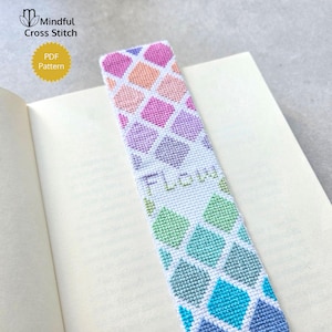 May include: A rectangular cross-stitch bookmark featuring a geometric diamond pattern in a gradient of colors transitioning from pink and orange at the top to green and blue at the bottom, with the word Flow stitched in light green thread.