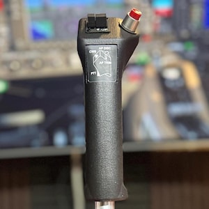 May include: A black and silver aircraft control stick with a red button on top. The stick has a textured grip and a metal shaft. The control stick has the text "CRS", "AP DISC", "AP TRIM", and "PTT".