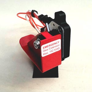Peut inclure: Levier rouge d'extension de train d'atterrissage d'urgence avec une base noire et une étiquette indiquant "EMERGENCY Gear Extension Max. 162 KIAS".