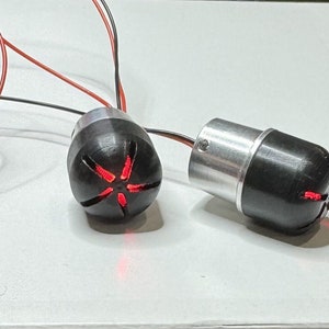 Könnte beinhalten: Zwei schwarze und silberne LED-Leuchten mit rot leuchtenden LEDs. Die Leuchten haben ein sternförmiges Design und sind durch Drähte verbunden.