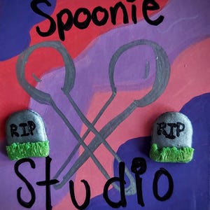 May include: A colorful artwork with the text "Spoonie Studio" and two crossed spoons. The background features red, purple, and blue abstract shapes. Two small tombstone-shaped objects with "RIP" are at the bottom.