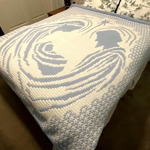 May include: A white and pale blue knitted blanket with a religious theme. The blanket shows silhouettes of figures and a star, with a detailed border. The design is a soft, textured knit, suitable for a bedspread or throw, measuring approximately 200cm x 200cm.