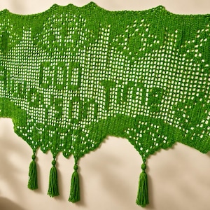 May include: A vibrant green, crocheted wall hanging with the words "Good Things" in a decorative font. The piece has a scalloped edge and is adorned with green tassels. The background is a neutral wall.