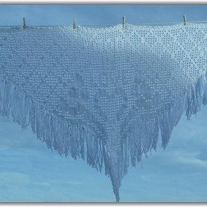 May include: A white crocheted shawl with fringe hanging on a washing line against a blue sky.