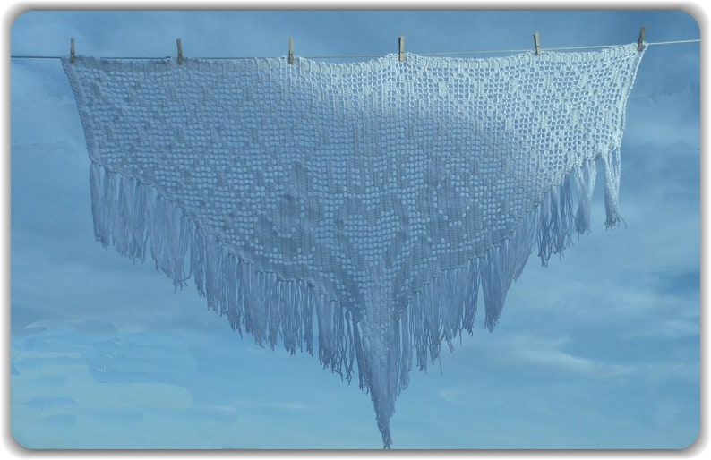 May include: A white crocheted shawl with fringe hanging on a washing line against a blue sky.