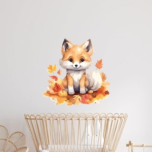 May include: A cute orange fox with a white chest and tail sitting on a bed of orange and brown leaves. The fox is smiling and has a white nose. The background is a white wall with a wooden floor.