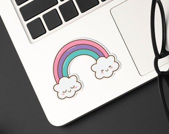 以下が含まれることがあります： 虹と笑顔の雲のステッカーが付いたノートパソコン。黒いフレームのメガネがトラックパッドに置かれています。キーボードは白文字と数字で表示されています。