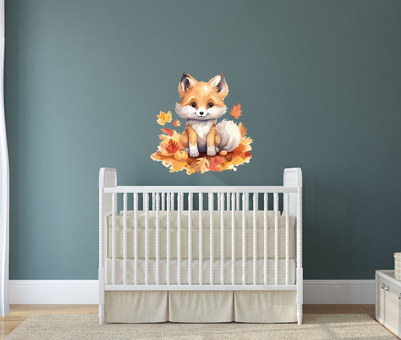 May include: A cute orange fox with a white chest and tail sits on a bed of orange and yellow leaves. The fox is looking at the camera with a friendly expression. The image is a nursery wall decal.