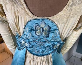 May include: A vintage white dress with a blue satin sash and embroidered floral detail.