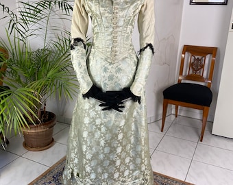 May include: A vintage, cream-colored, long-sleeved dress with a floral pattern and a black lace collar. The dress has a fitted bodice and a full skirt with a gathered hem.