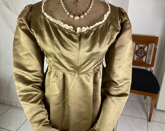 Puede incluir: Un vestido largo de satén verde oliva de manga larga con un ribete de encaje alrededor del escote. El vestido está en un maniquí y tiene un collar de perlas alrededor del cuello.