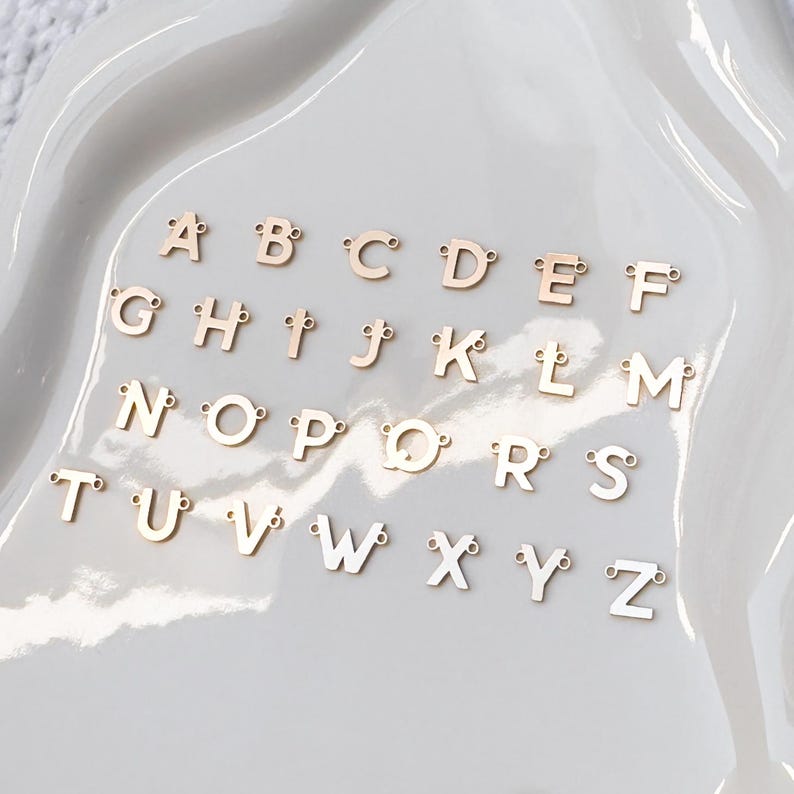 May include: A set of gold-colored metal alphabet letter charms. Each letter is separate and has a small loop for attaching to a necklace, bracelet, or other jewelry.