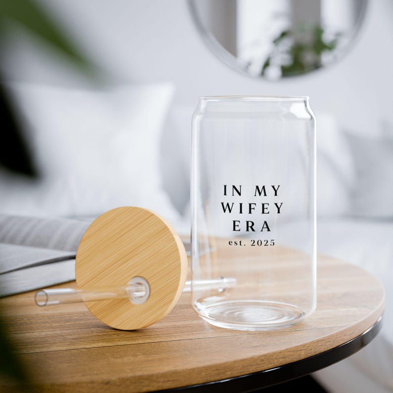 May include: A clear glass can with a bamboo lid and a straw. The can has the text "In My Wife Era est. 2025" printed on it.